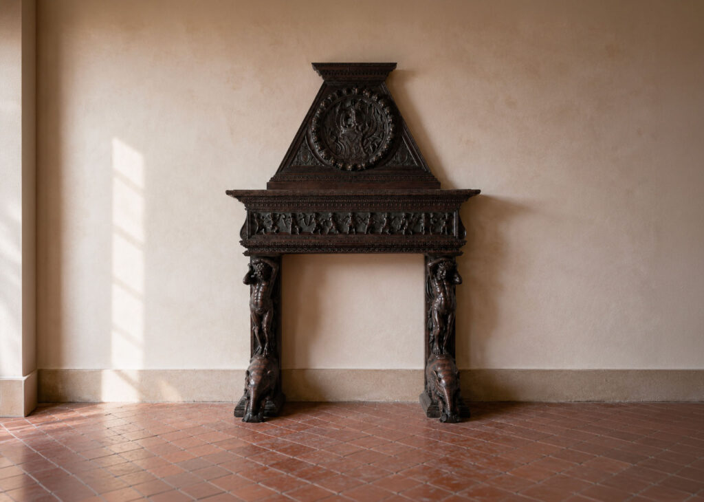 Importante camino emiliano del XIX secolo in legno di noce riccamente intagliato con telamoni, elefanti, putti musicanti e stemma con drago alato. Trattato da Gregory's Casa d'Aste Bologna, prima casa d'aste di Bologna dal 2013.