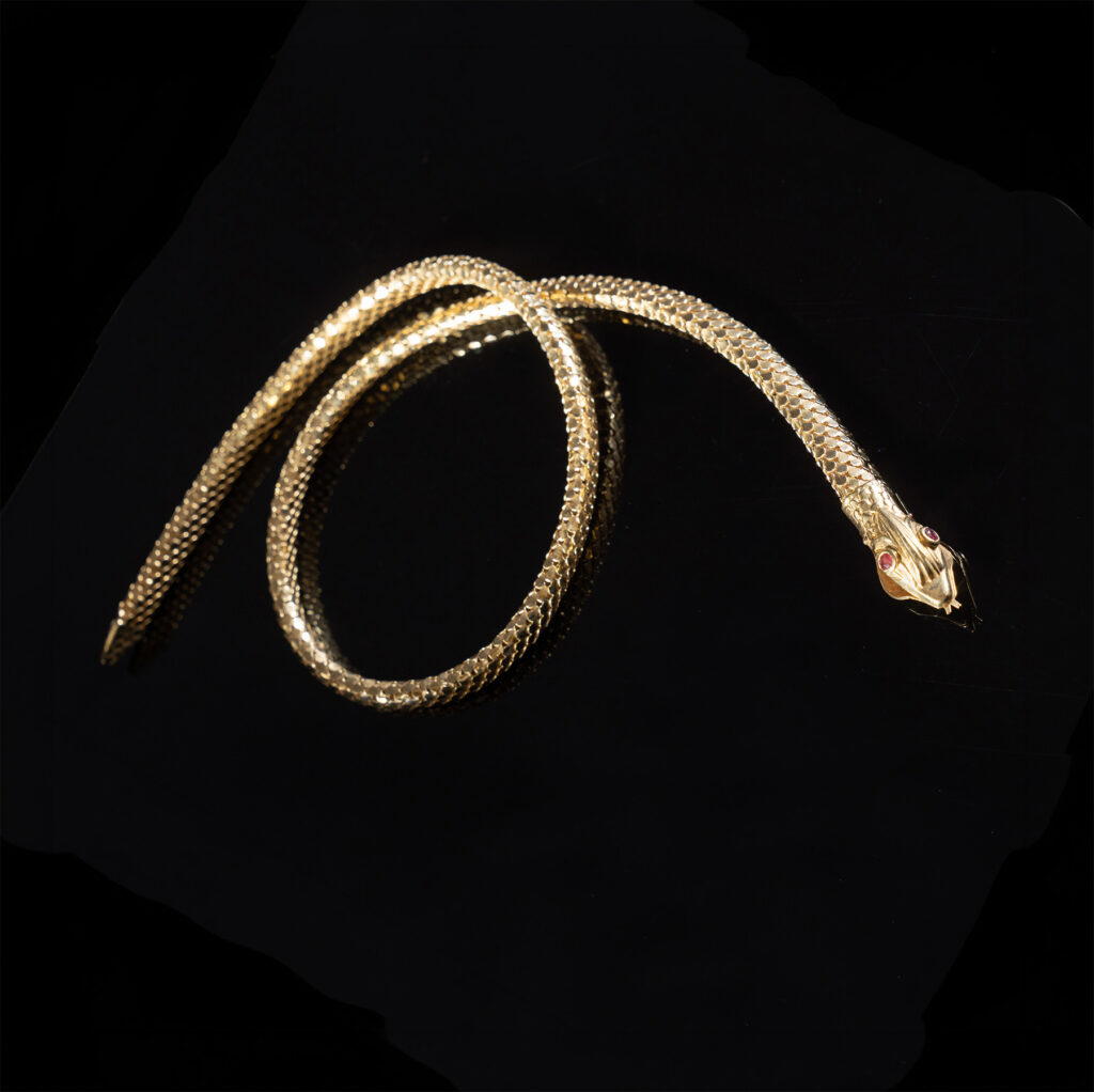 Collier tubolare in oro giallo 18 kt terminante con testa di serpente decorata da due rubini.