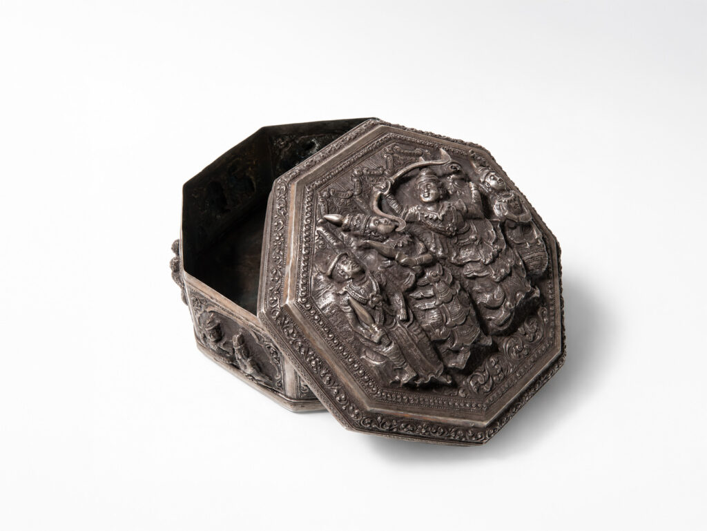 Contenitore ottagonale birmano in argento sbalzato con coperchio decorato da figure in rilievo e motivi floreali, XIX secolo.
