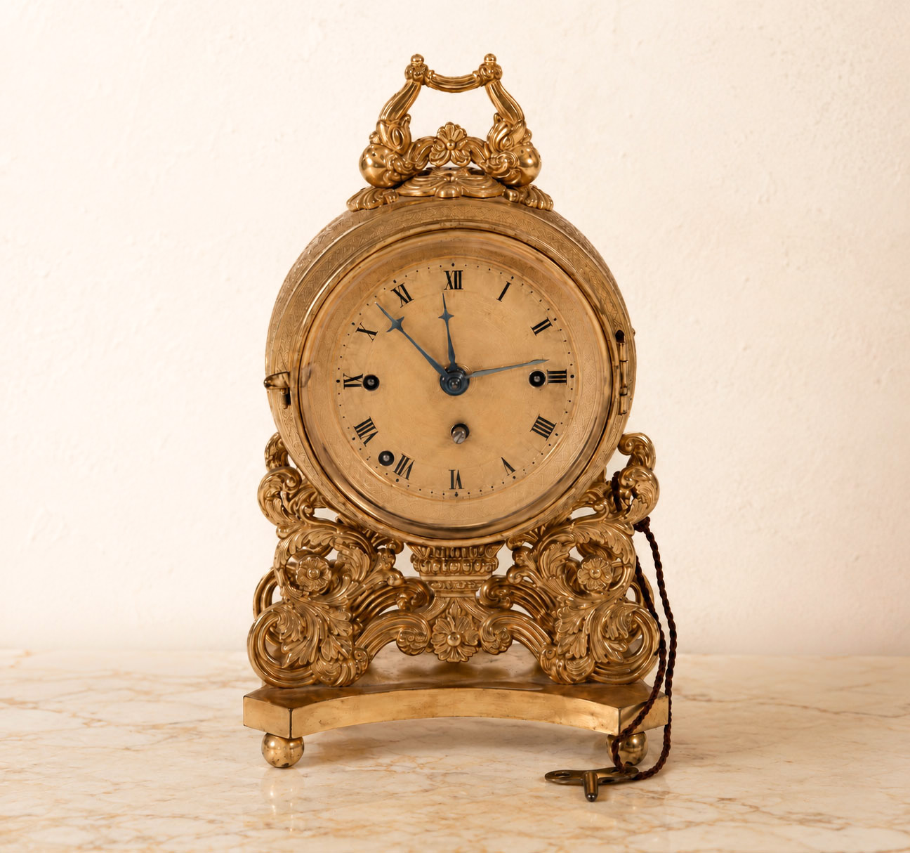 Orologio da tavolo in bronzo dorato del XIX secolo a carica con chiavetta, quadrante con numeri romani e ricca decorazione rocaille.