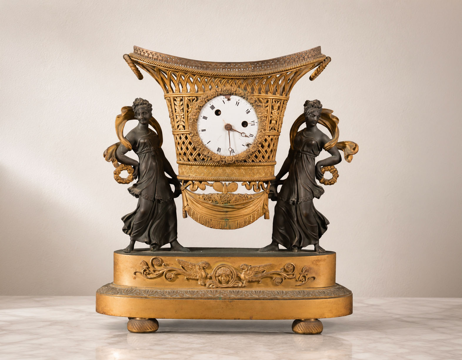 Orologio da tavolo del XIX secolo in bronzo dorato con corbeille sostenuta da due muse in bronzo patinato e quadrante in smalto con numeri romani.